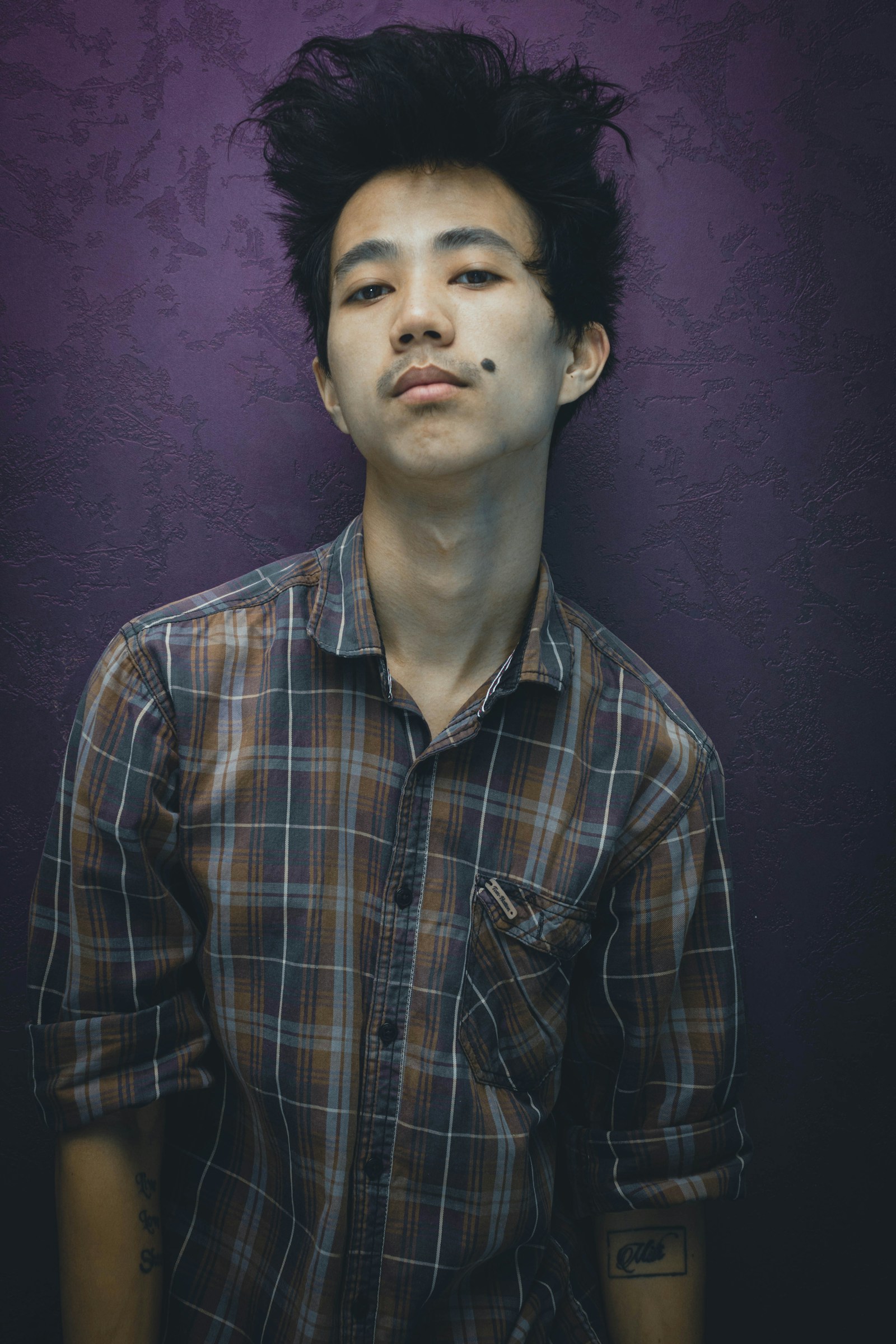 Brown and blue checked button-up shirt worn against a plum wall.