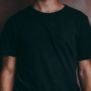 Plain black crew-neck T-shirt worn against a warm brown background.