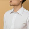 White collared cotton shirt, worn against a warm neutral background.