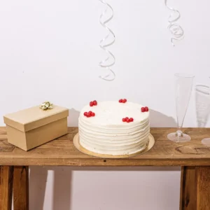 A white celebration cake, closed gift box and two glasses on a wooden table.