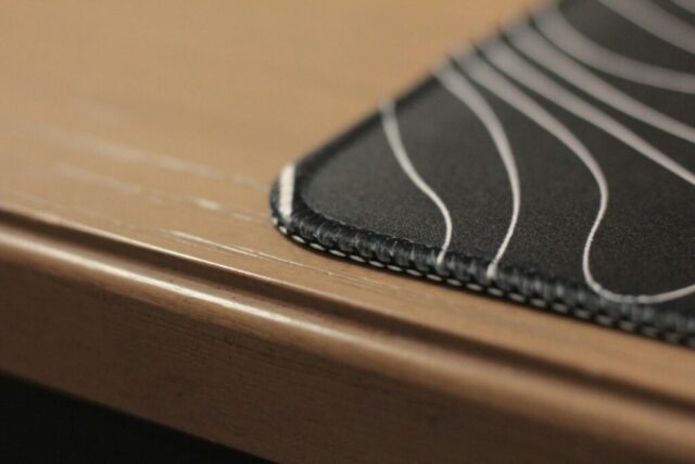 Close-up of the stitched edge of a charcoal desk mat with a light contour pattern.