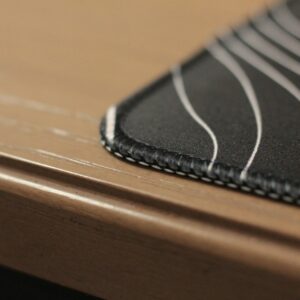 Close-up of the stitched edge of a charcoal desk mat with a light contour pattern.