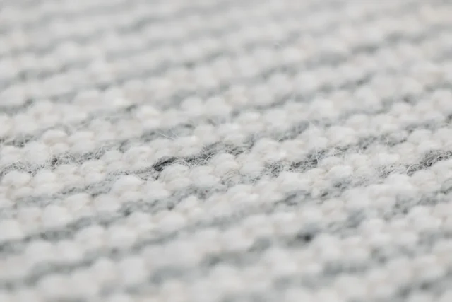 Close-up view of a grey handmade woolen rug texture showing detailed weave.