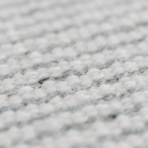 Close-up view of a grey handmade woolen rug texture showing detailed weave.