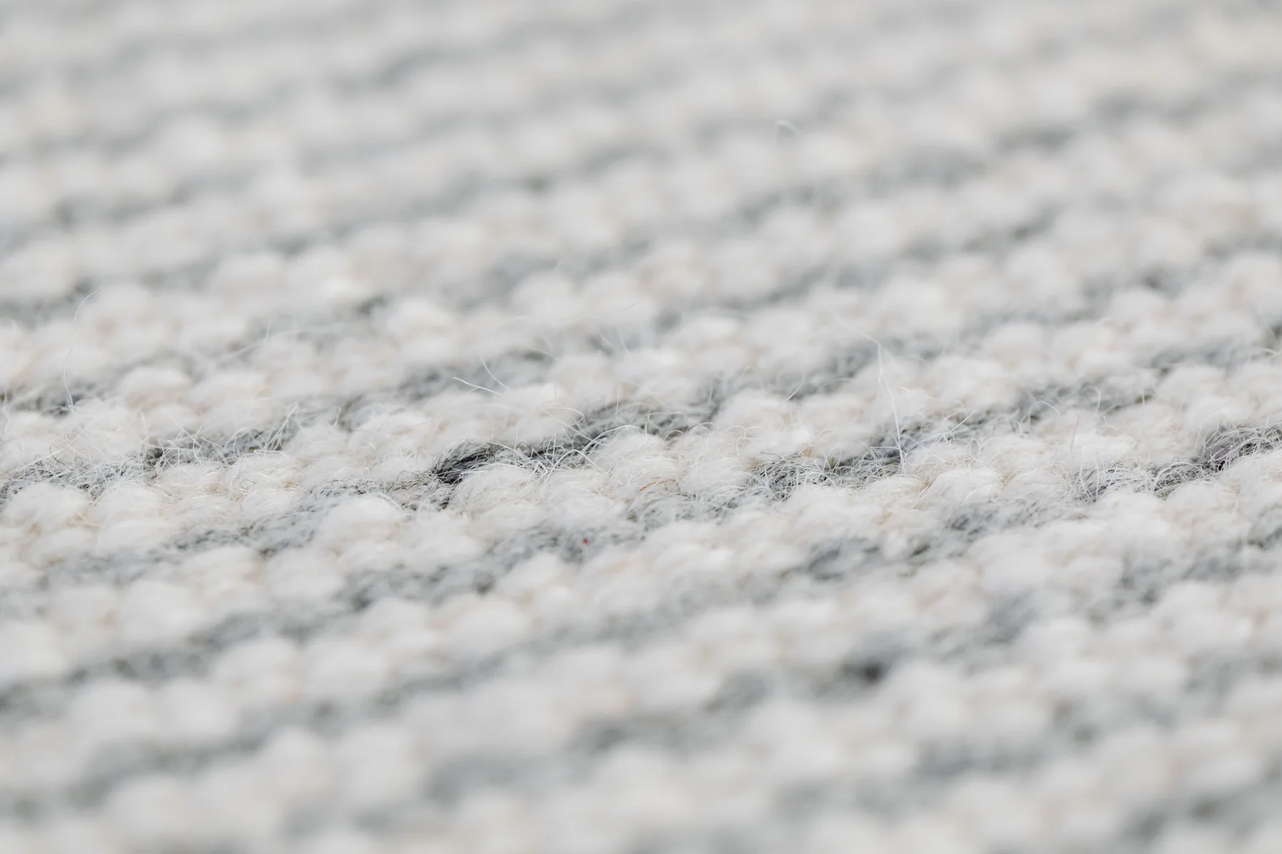 Close-up view of a grey handmade woolen rug texture showing detailed weave.