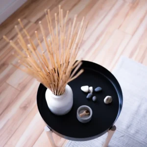 Round table with minimalist decor in Japandi style, featuring vase with sticks and stones.