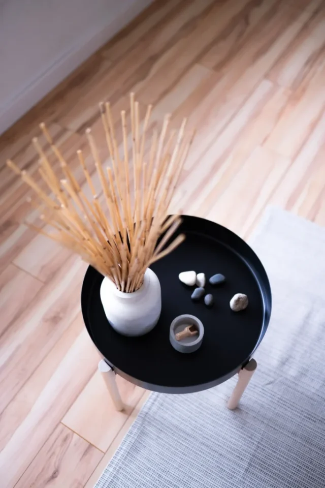 Round table with minimalist decor in Japandi style, featuring vase with sticks and stones.