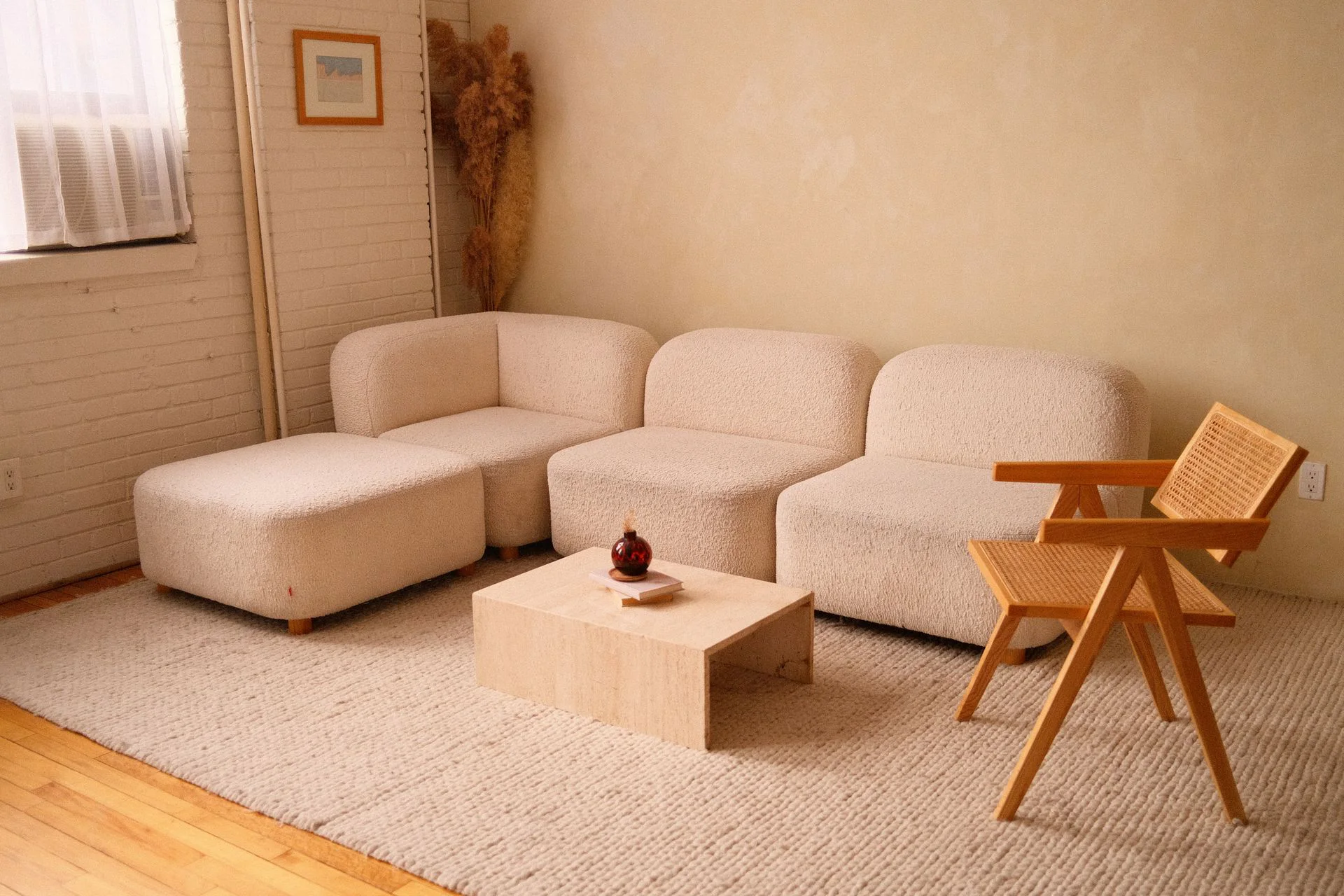 Warm living room with a cream bouclé sofa, timber lounge chair and low stone table