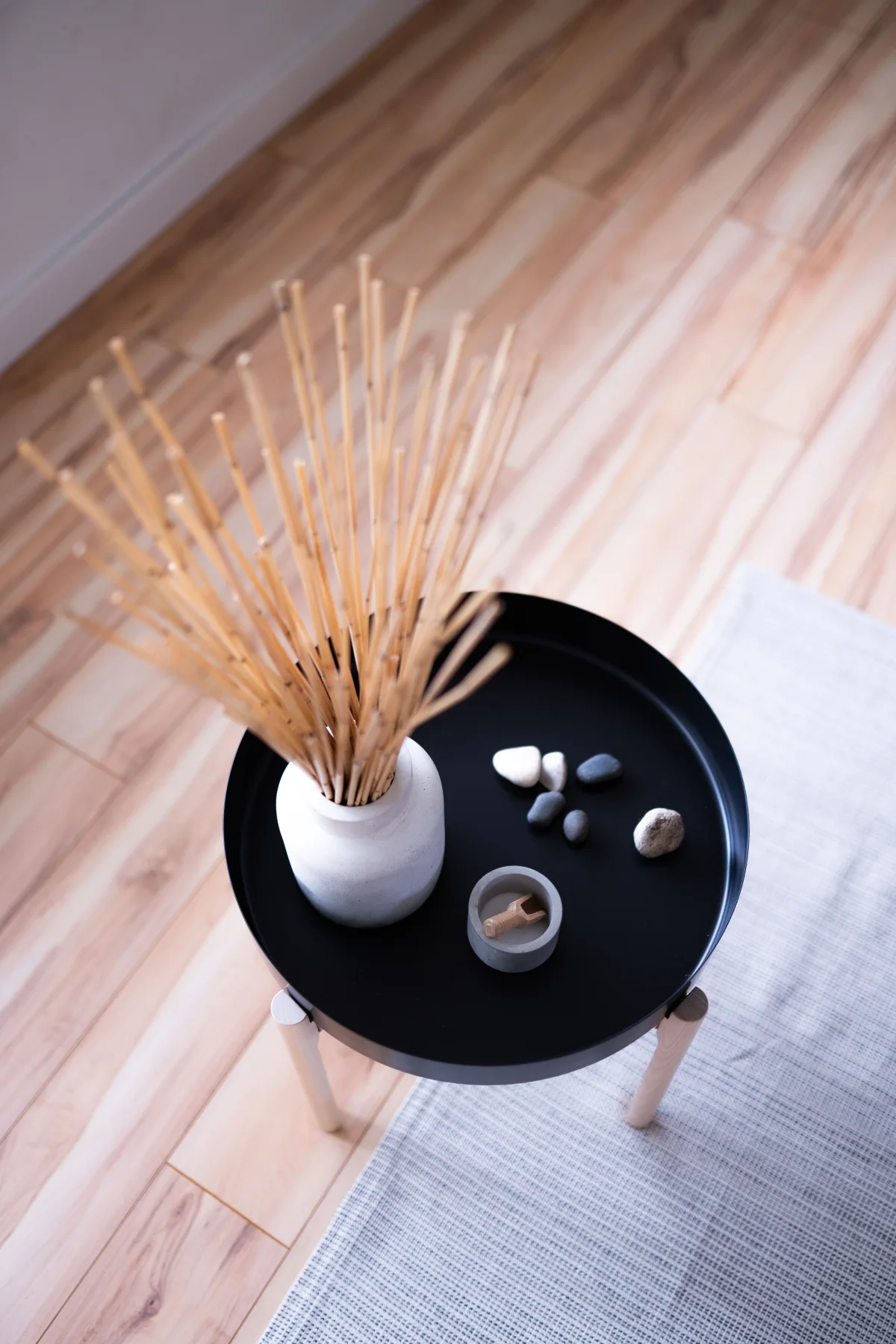 Round table with minimalist decor in Japandi style, featuring vase with sticks and stones.